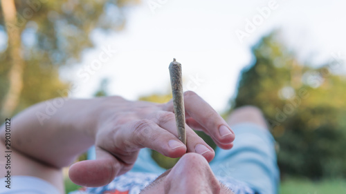 The young person smoking medical marijuana joint outdoors. The young man smoke cannabis blunt, close-up.