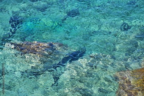 Turquoise sea water with grey natural stones. Purity ripple ocean water surface with selective focus and sun light. Transparent blue water surface with rocks. Caribbean water background. Halkidiki