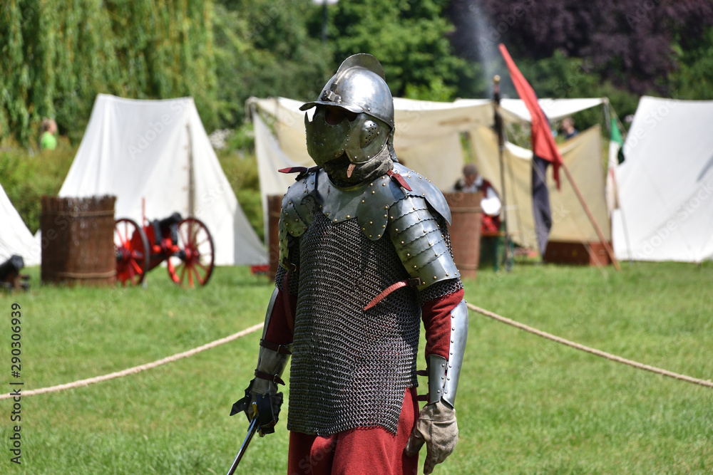 Knight in a chainmail with a sabre and lobster-tailed pot helmet. Historical reenactment of a medieval knight fights in Brodnowski park in Warsaw, Poland Knight in a chainmail with a sabre and lobster-tailed pot helmet. Historical reenactment of a medieval knight fights in Brodnowski park in Warsaw, Poland