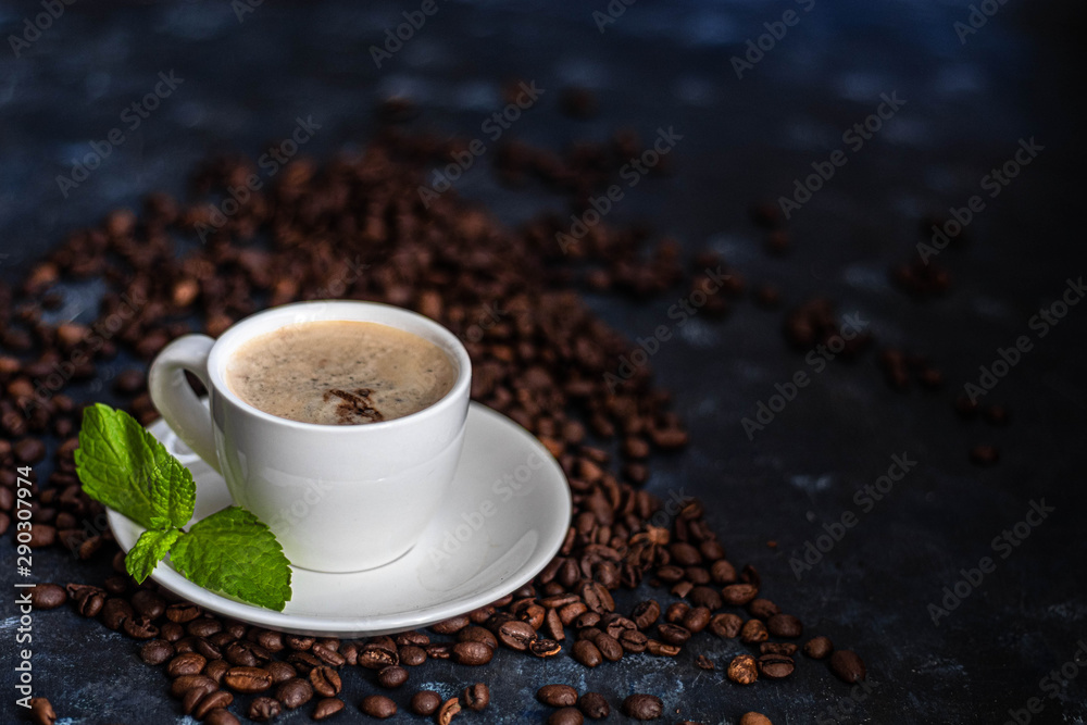Obraz premium A cup of delicious, aromatic coffee. It is on a substrate of coffee beans. Has a lush, white foam. Decorated with mint leaves.
