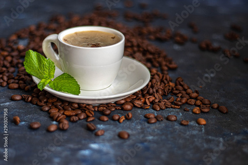 A cup of delicious, aromatic coffee. It is on a substrate of coffee beans. Has a lush, white foam. Decorated with mint leaves. 