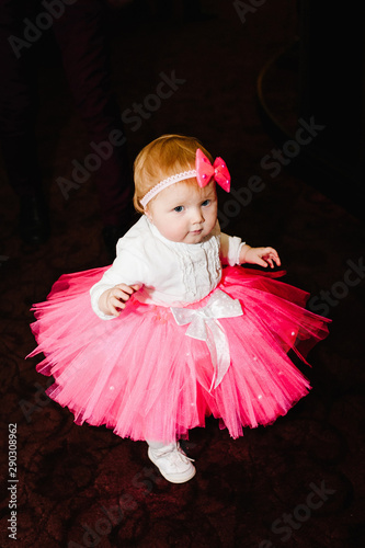 Surprised cute little beautiful, gentle baby girl, happy princess with a bow on her head in a skirt with tulle. Birthday fashionable kid looking to camera. Expressing true emotions.