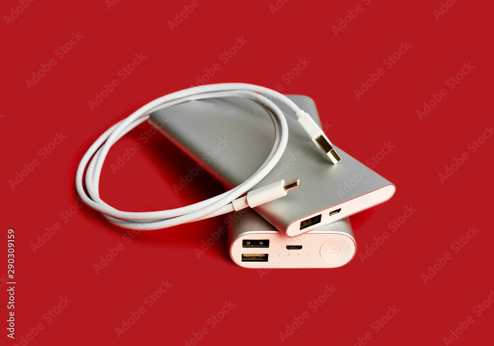 Obraz premium Power bank for charging mobile devices. White smart phone charger with power bank. Battery bank on a red background . External battery for mobile devices.