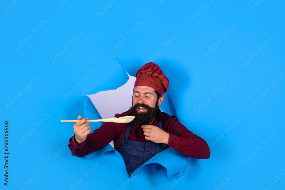Bearded man chef preparing to cook food. Handsome chef cook with kitchen utensils. Chief man in cook uniform with wooden spoon looking through paper. Bearded cook holds wooden kitchen cooking tools. Bearded man chef preparing to cook food. Handsome chef cook with kitchen utensils. Chief man in cook uniform with wooden spoon looking through paper. Bearded cook holds wooden kitchen cooking tools.