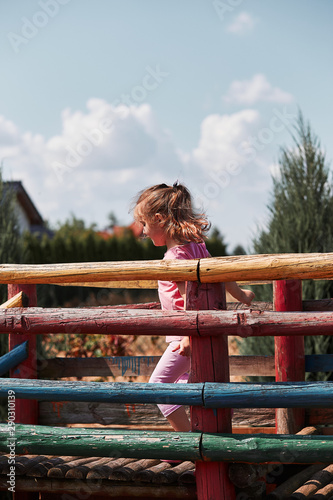 Little adorable girl playing in a home playground in a backyard. Happy smiling kid having fun on a play house on summer day. Real people, authentic situations