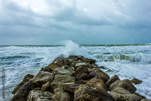 Crashing waves on a stony groyne (breakwater) during a massive storm under a grey sky photo