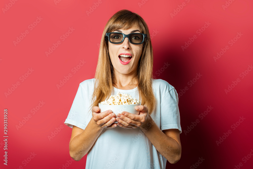Young beautiful woman in glasses for watching movies and popcorn on a pink background. The concept of watching a movie, movie news, cinema, rating Young beautiful woman in glasses for watching movies and popcorn on a pink background. The concept of watching a movie, movie news, cinema, rating