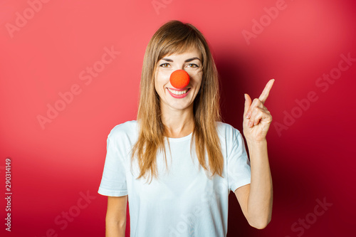 Fényképezés Young beautiful woman with a red nose of a clown on a pink background