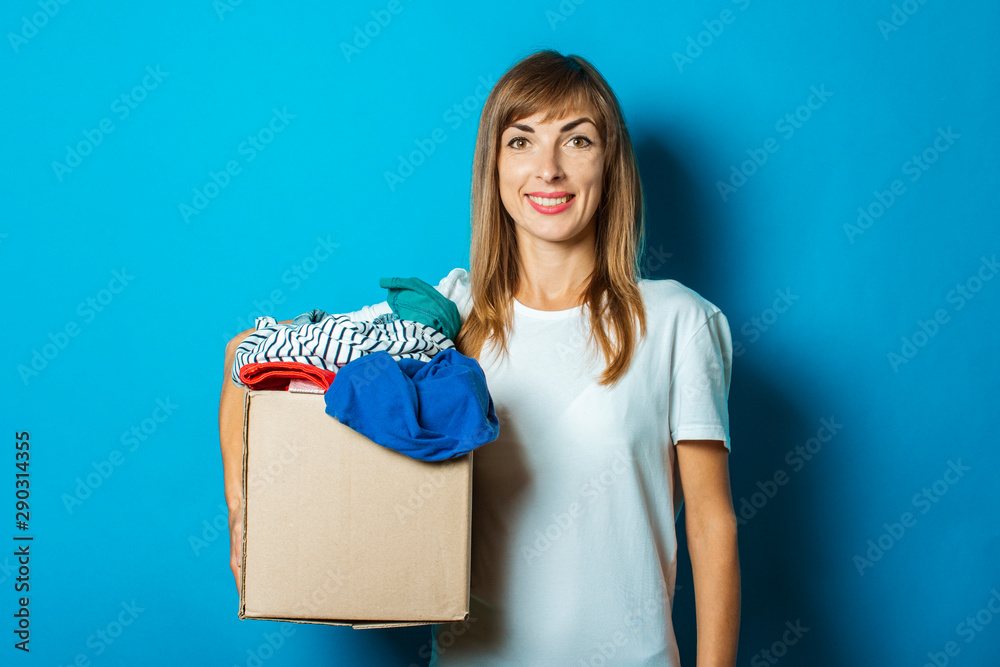 Young woman holds a cardboard box with things on a blue background. Donation concept Young woman holds a cardboard box with things on a blue background. Donation concept