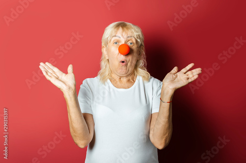 Funny old woman with a red nose of a clown on a pink background. Concept red nose day, holiday, party, clown