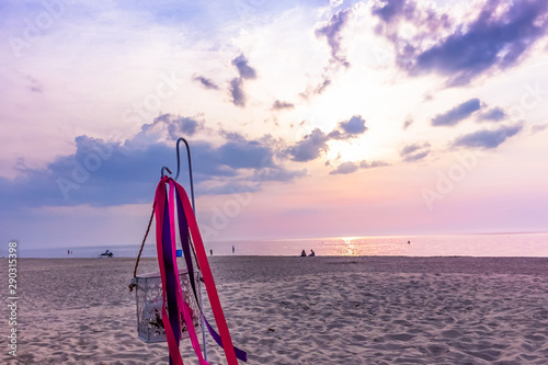 décor with colorful ribbons on the sandy beach by the sea, a peaceful sunset evening with colorful skies and clouds  people silhouettes by the sea © Dainis
