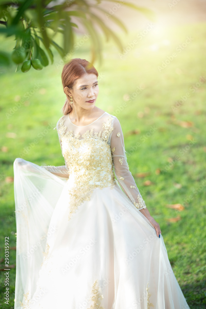 Beautiful portraits with natural light asian woman bride in wedding dress in nature meadow flower,standing in green grassy field in background.