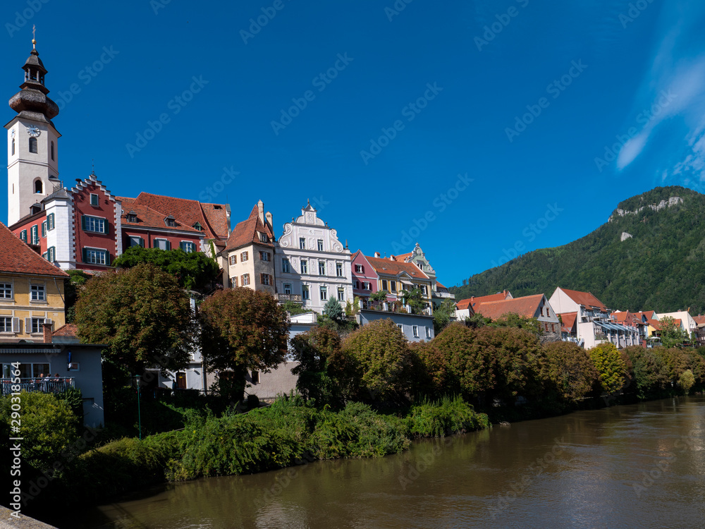 Flusseitige Silouhette  von Frohnleiten an der Mur im Bezirk Graz, Österreich mit blauem Himmel, Kirche und historischen Häusern
