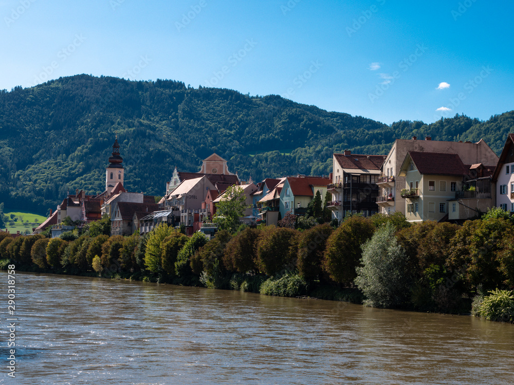 Flusseitige Silouhette  von Frohnleiten an der Mur im Bezirk Graz, Österreich mit blauem Himmel, Kirche und historischen Häusern