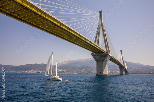 Sailboat passes under the Rio Antirrio Bridge or Charilaos Trikoupis Bridge  photo taken from the boat in summer sunny day.