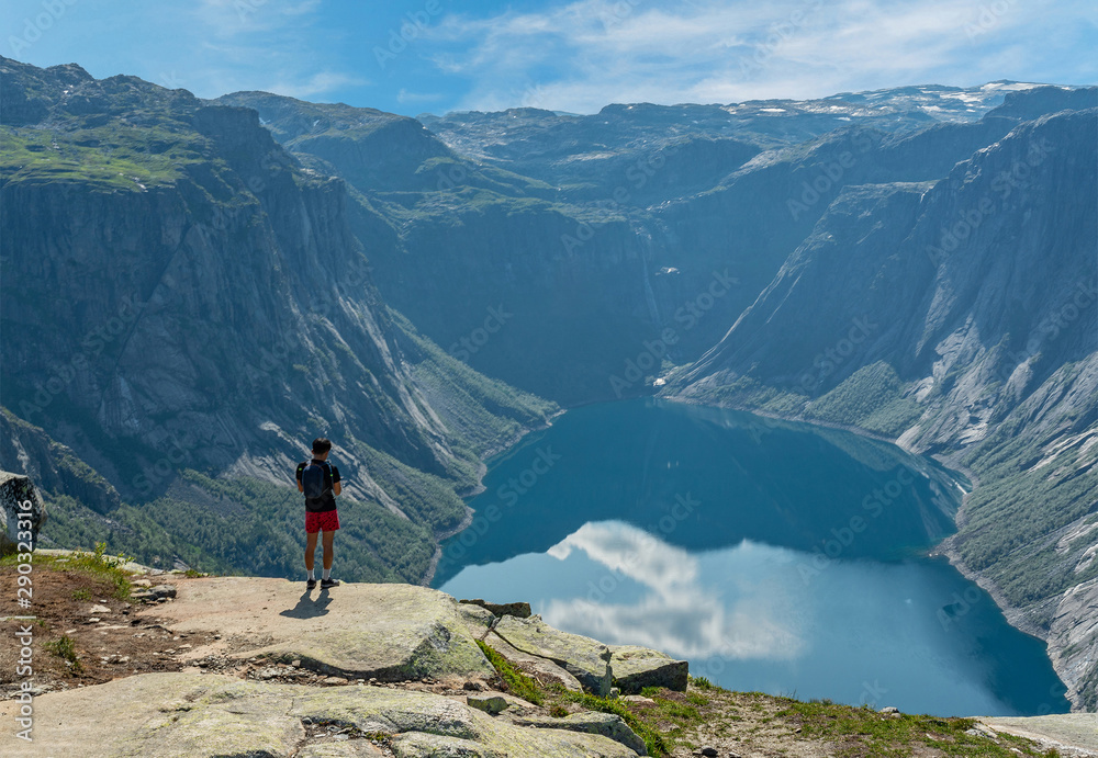Mountain lake landscape, Norway. Young man standing on the shore of Ringedalsvatnet lake. Way to Trolltunga rock.