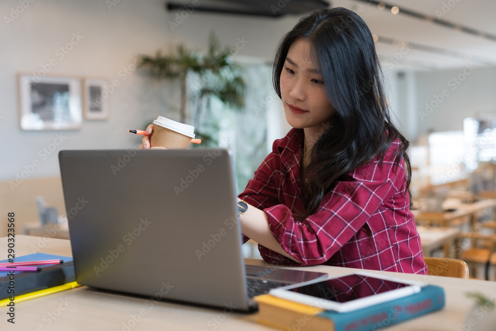 Close up of young business woman sitting at table and taking notes in notebook while holding coffee cup in her hand Close up of young business woman sitting at table and taking notes in notebook while holding coffee cup in her hand