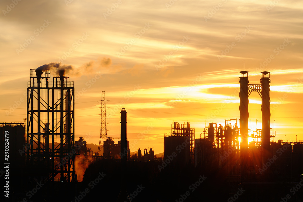 Petrochemical plant or oil and gas refinery industry with smoke stacks in silhouette image on orange sky sunset background