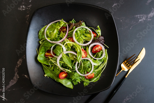 Eat green concept with organic fresh vegetable salad in ceramic plate on black background.