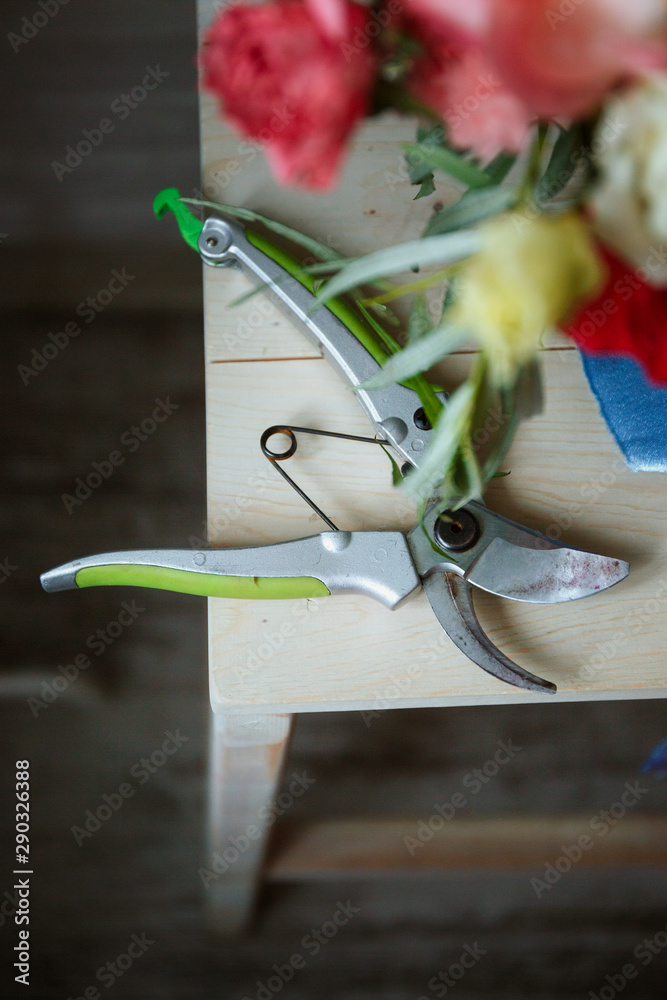 Secateurs on a wooden background next to greens and flowers. Concepts of floristry, bouquet assembly, floristry, handmade details