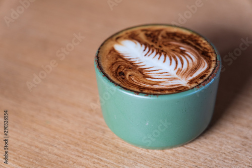 Cappuccino coffee with latte art milky foam on wooden table background.