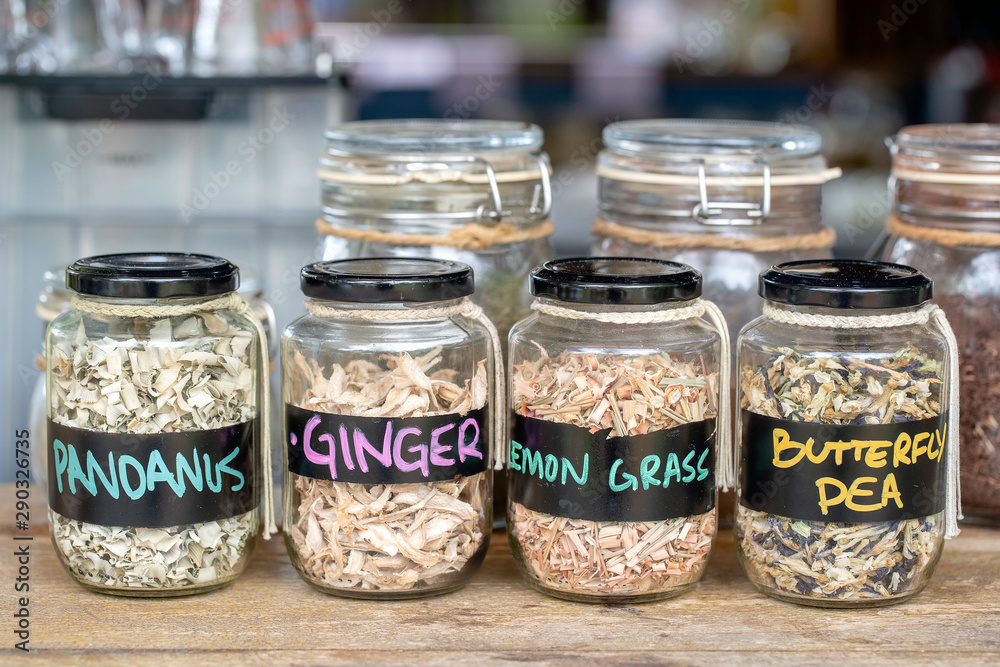 Assortment of dried spices in glass bottles on wooden background. Dry ginger, pandanus, lemon grass and butterfly pea in glass jars Assortment of dried spices in glass bottles on wooden background. Dry ginger, pandanus, lemon grass and butterfly pea in glass jars