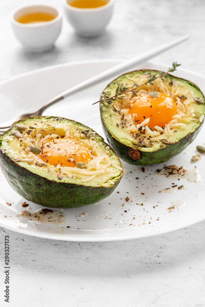 Tasty and healthy avocado snack. Slices of avocado with raw yolk, cheese, olive oil and spices on a white plate close-up. Tasty and healthy avocado snack. Slices of avocado with raw yolk, cheese, olive oil and spices on a white plate close-up.