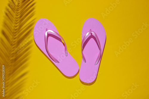 Tropical beach lifestyle. Flip flops and shadow from a palm leaf on yellow background. Summer background. Top view
