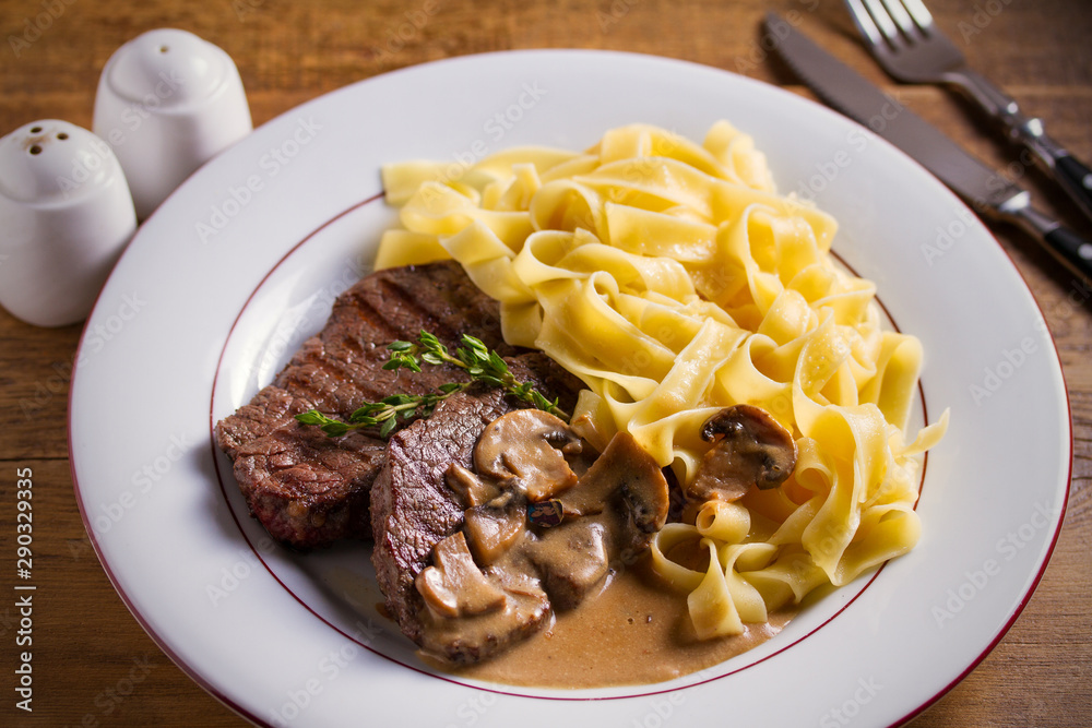 Grilled beef steaks and noodles in creamy mushroom sauce, garnished with thyme on white plate Grilled beef steaks and noodles in creamy mushroom sauce, garnished with thyme on white plate