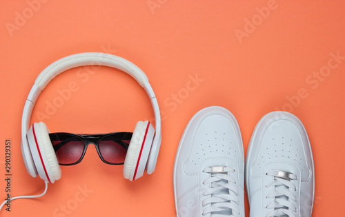 White Sneakers and headphones with sunglasses on coral color background. Casual design. Music concept. Flat lay, minimal.