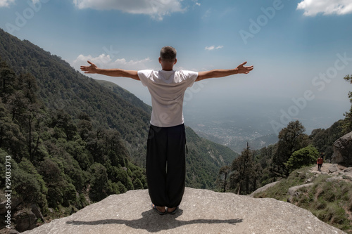 I am free! A man stands on top of a cliff with his arms outstretched to the sides. Back view.