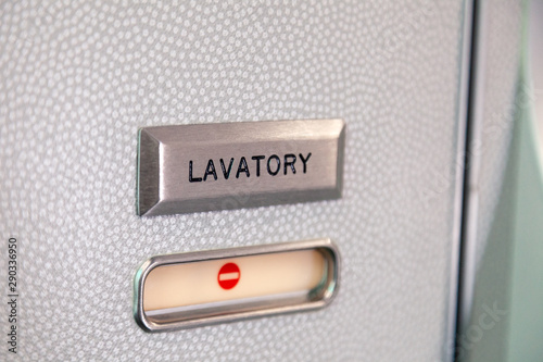 Vacant red sign, occupied symbol on an airplane lavatory door. Raised, brushed metal lavatory sign, recessed plastic vacant sign. Toilet room, wc, closet on airplane board