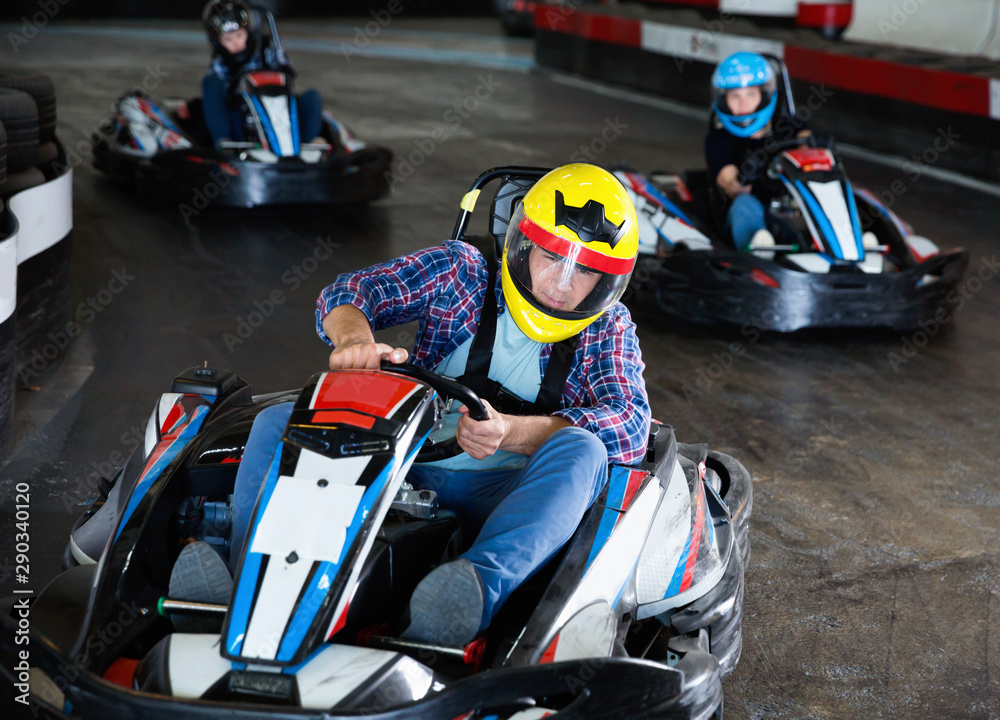 Male in helmet  and other people driving cars for karting in sport club indoor