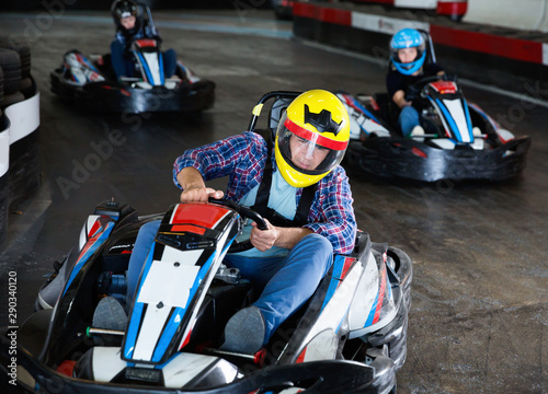 Male in helmet and other people driving cars for karting in sport club indoor