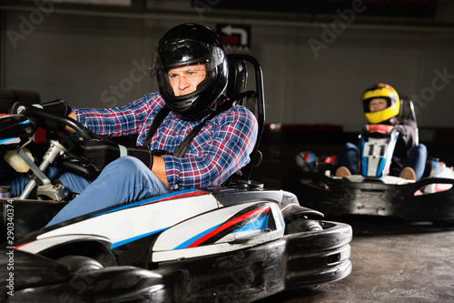 Male in helmet  and other people driving cars for karting in sport club indoor © JackF