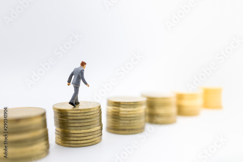 Business, Money, Finance and management concept. Close up of businessman miniature figure walking on top of stack of gold coins on white background.