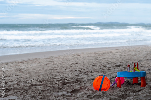 Toys on beach, blue sea, white sea foam, blue sky, blurred background.