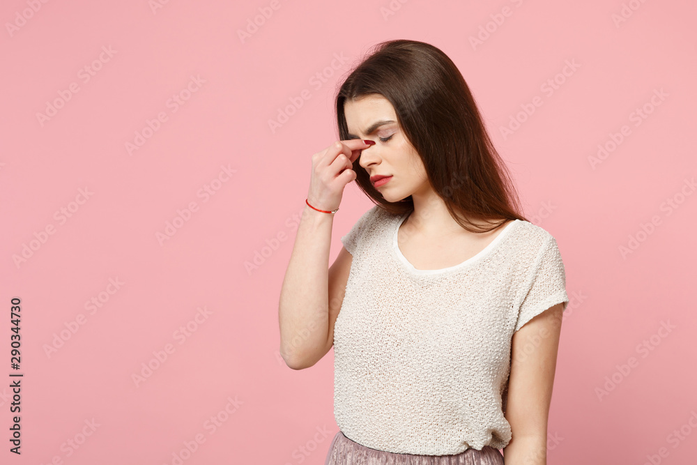 Tired young woman in casual light clothes posing isolated on pink background, studio portrait. People sincere emotions lifestyle concept. Mock up copy space. Keeping eyes closed, putting hand on nose.
