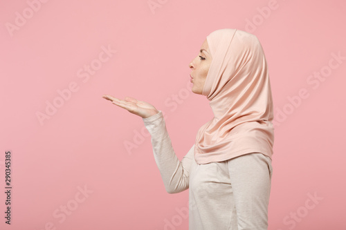 Fotografie Side view of arabian muslim girl in hijab light clothes posing isolated on pink wall background studio portrait
