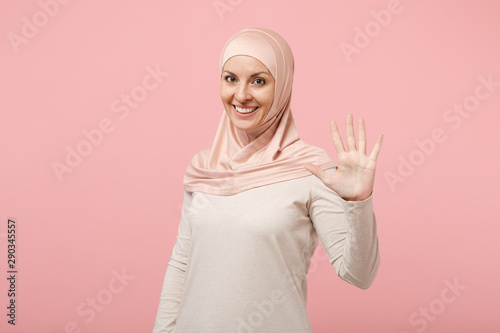 Smiling young arabian muslim woman in hijab light clothes posing isolated on pink background. People religious Islam lifestyle concept. Mock up copy space. Showing palm, making high five with hand.