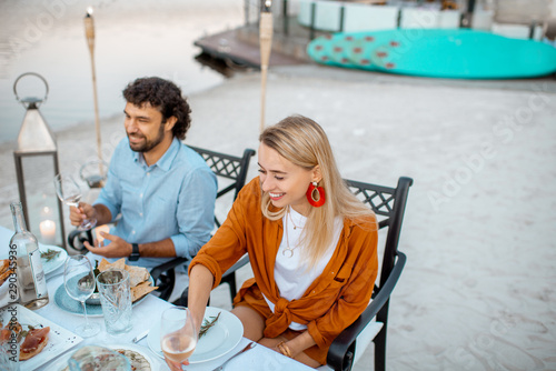 Young couple dinning with friends at the beautifully decorated table on the beach near the lake