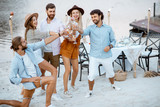 Group of young friends having fun, clinking wine glasses during a festive party on the beach with dinning table on the background
