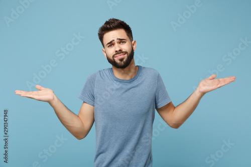 Young confused man in casual clothes posing isolated on blue wall background, studio portrait. People sincere emotions lifestyle concept. Mock up copy space. Spreading and pointing hands aside.