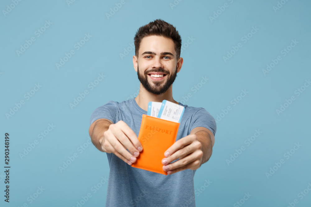 Young smiling cheerful man in casual clothes posing isolated on blue wall background, studio portrait. People lifestyle concept. Mock up copy space. Holding in hands passport, boarding pass tickets. Young smiling cheerful man in casual clothes posing isolated on blue wall background, studio portrait. People lifestyle concept. Mock up copy space. Holding in hands passport, boarding pass tickets.