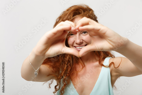 Young smiling redhead woman girl in casual light clothes posing isolated on white background in studio. People lifestyle concept. Mock up copy space. Showing shape heart with hands, heart-shape sign.
