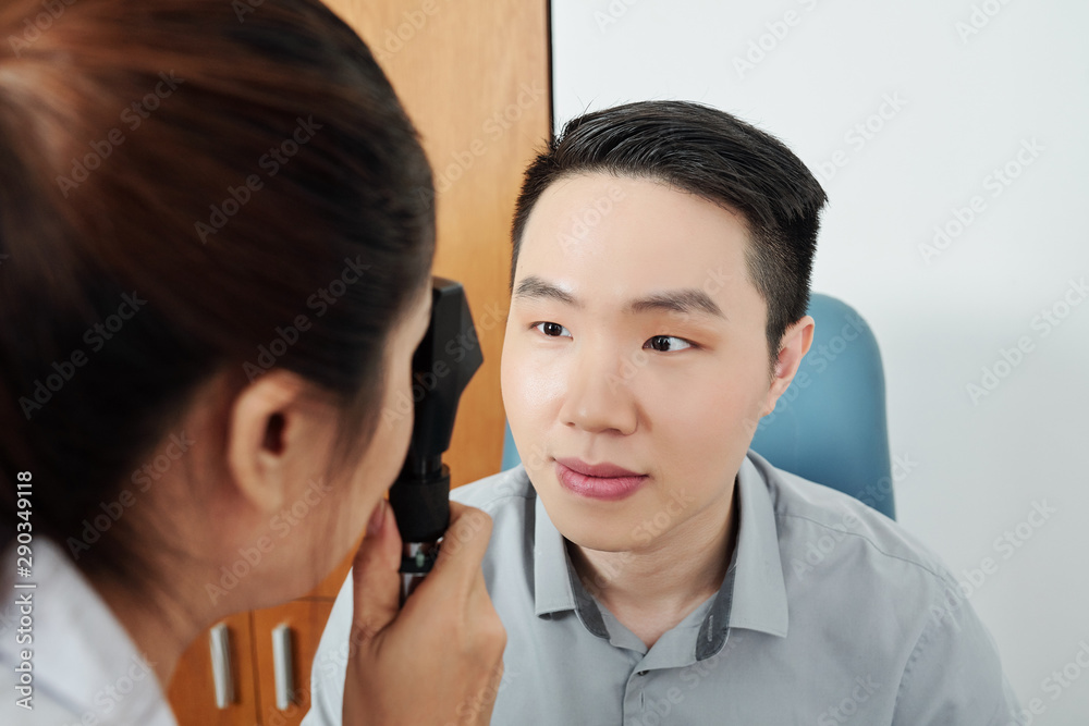 Female doctor examining the eyesight of her Asian patient while he visiting the hospital Female doctor examining the eyesight of her Asian patient while he visiting the hospital