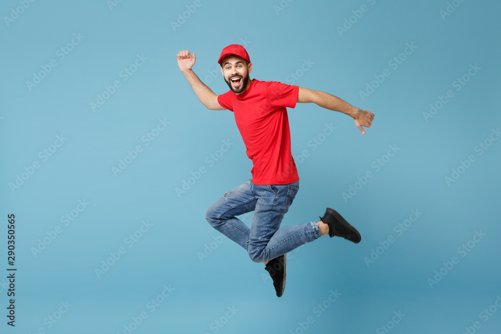 Delivery man in red uniform workwear isolated on blue wall background, studio portrait. Professional male employee in cap t-shirt print working as courier dealer. Service concept. Mock up copy space. Delivery man in red uniform workwear isolated on blue wall background, studio portrait. Professional male employee in cap t-shirt print working as courier dealer. Service concept. Mock up copy space.