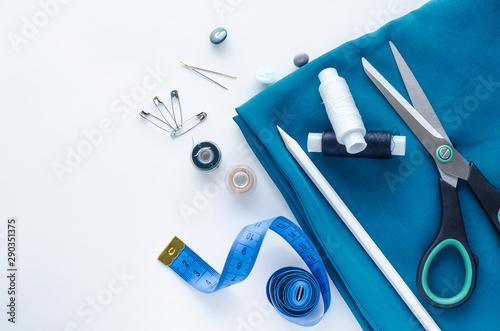 Desktop Accessories for sewing on a white background. Roll of blue satin fabric, tape measure, scissors, needles. Fashion, Design studio for tailoring, atelier concept.  Flat lay, top view, copy space
