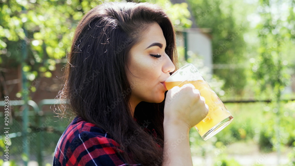 Portrait of young happy woman drinks beer from glass, quenches thirst, in the garden at a barbecue party