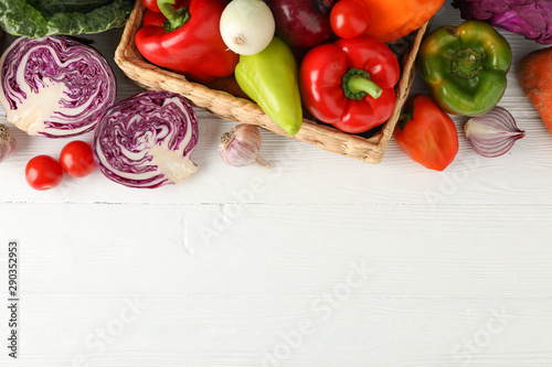Wicker basket and vegetables on white wooden background, top viewWicker basket and vegetables on white wooden background, top view